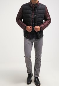 Vadderad jacka med svart kropp, bordeauxfärgade ärmar, tryckknappstängning och quilterad textur. Grå byxor och svarta skor fulländar outfiten.