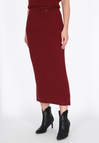 Burgundi ribbed kötött midi szoknya magas derékkal, fekete stiletto bokacsizmával párosítva, amelynek hegyes orra és kivágott dizájnja van.