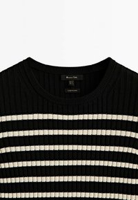 Zwart-witte geribbelde gebreide trui met horizontale strepen, ronde halslijn en een label zichtbaar aan de binnenkant van de kraag.