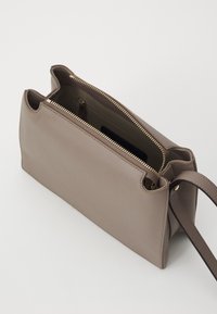 Kožna torba u taupe boji s teksturiranom završnom obradom. Ima gornje zatvaranje na zip i podesivu naramenicu. Unutrašnjost uključuje zip džep.