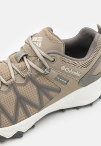 Sneaker sportivo beige con tomaia in mesh e sintetico. Presenta accenti grigi, sovrapposizioni testurizzate e una suola intermedia bianca con suola esterna stampata.