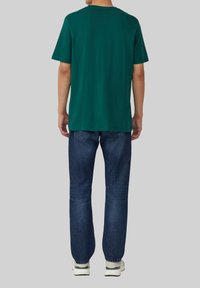 Groen katoenen T-shirt met korte mouwen en een ronde hals, gecombineerd met donkerblauwe rechte jeans en witte sneakers.