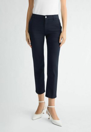 Navy blue pants with a slim fit, straight legs, front pockets, and a single button closure, paired with white, pointed-toe heels.