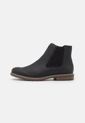Bottine en cuir noir avec panneaux latéraux élastiques, détails brogue, talon empilé marron et semelle cousue sur fond blanc.