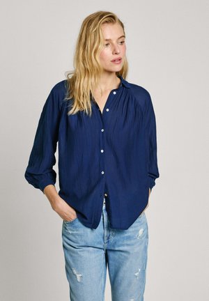 Navy blue button-up shirt with a relaxed fit, long sleeves, and textured fabric. Worn with light blue distressed jeans.