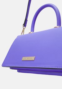 Fioletowa syntetyczna torebka o zwartej konstrukcji, z teksturowaną powierzchnią, złotymi ozdobami i podwójnymi uchwytami oraz odpinanym paskiem.
