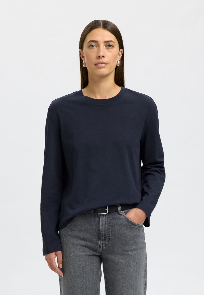 Navy duga majica s dugim rukavima od mekanog tkanina, s okruglim izrezom i ležernim krojem, u kombinaciji sa sivim visokim trapericama.