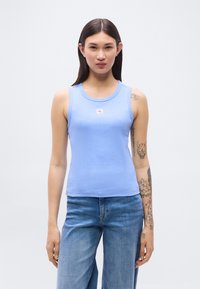 Φωτεινό γαλάζιο ριπ μανίκι τοπ με στρογγυλή λαιμόκοψη και μικρό λογότυπο. Συνδυασμένο με τζιν παντελόνι σε χαλαρή εφαρμογή.