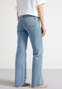 Ljust blå denimjeans med en rak bendesign, som har två bakfickor och en texturerad yta. Tyget har en urblekt look.