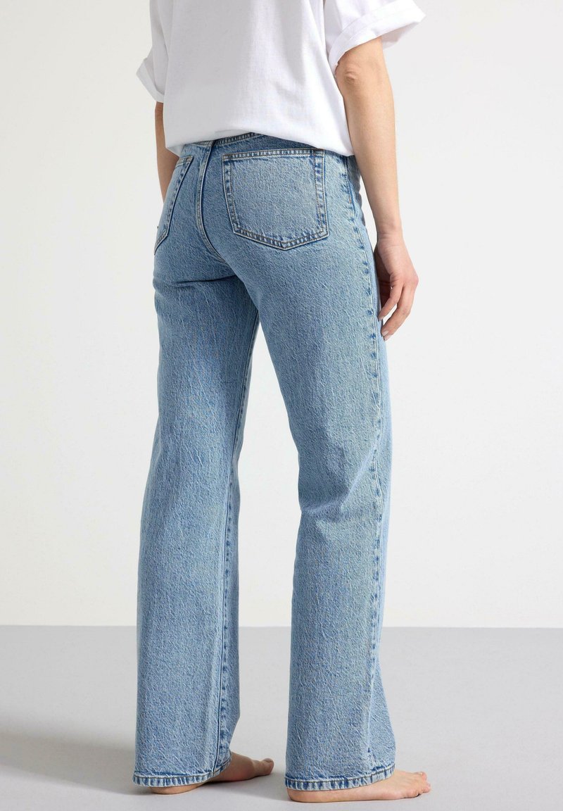 Ljust blå denimjeans med en rak bendesign, som har två bakfickor och en texturerad yta. Tyget har en urblekt look.