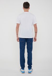 T-shirt bianco in cotone con maniche corte, abbinato a jeans in denim blu con tasche posteriori e cuciture a contrasto. Calzature comode.