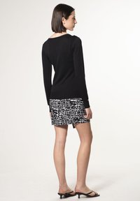 Schwarzes langärmliges Oberteil, kombiniert mit einem schwarz-weiß gemusterten Miniröckchen. Das Outfit hat eine schmale Passform mit einer glatten Textur und einem einfachen Design.