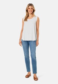 Weißes ärmelloses Oberteil mit rundem Halsausschnitt, kombiniert mit hellblauen Jeans und braunen Sandalen. Einfaches Design, keine sichtbaren Muster oder Beschläge.