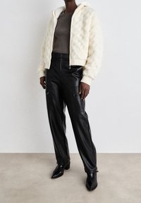 Krämfärgad vadderad bomberjacka med huva, i kombination med svarta lädercargo-byxor med sidofickor och dragkedjor. Svarta spetsiga anklar.