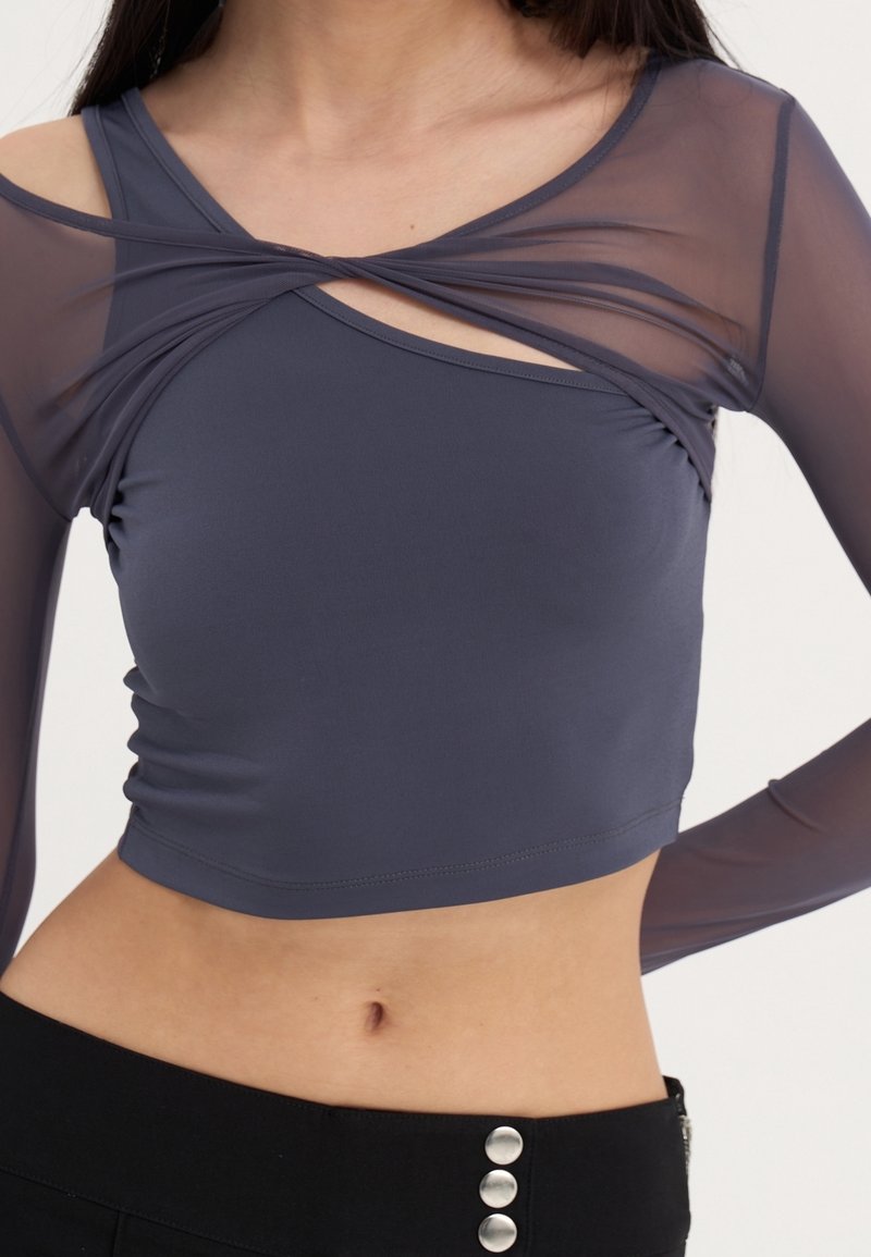 Blå kort topp med långa genomskinliga ärmar, med en tvinnad design fram och rynkor på sidorna. Slät tyg med en figurnära silhuett.