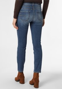Mörkblå denimjeans med slim fit, med bakfickor med dragkedjor. Matchas med bruna mockaskor vid ankeln. Slät textur.