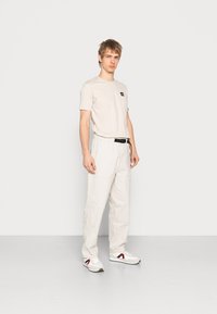 Beige t-shirt with a logo on the chest, paired with light-colored cargo pants and white sneakers featuring red accents.