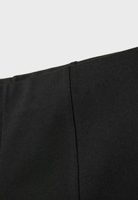 Pantalons noirs taille haute en matériau lisse et extensible avec un léger brillant, présentant une taille épurée et des détails sur les coutures latérales.