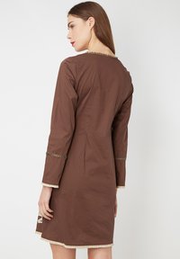 vestido marrón a la altura de la rodilla con mangas largas, que presenta un borde texturizado en las mangas y el dobladillo, y un sutil detalle en el escote trasero.