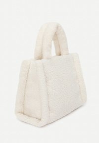 Kleine cremefarbene Handtasche mit einer weichen, flauschigen Textur und einer strukturierten, dreieckigen Form mit zwei kurzen Griffen.