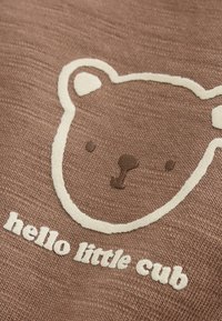 Brown fabric with a simple white and brown bear face outline and the text "hello little cub" below it.