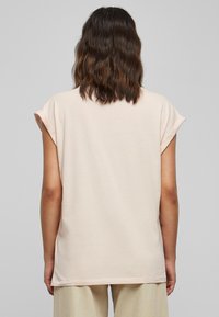 Hele roosa, lühikeste varrukatega T-särk, mis on lahtise lõikega ja mille varrukad on üles rullitud, valmistatud pehmest kangast. Tagakülje vaade, sirge äärega.