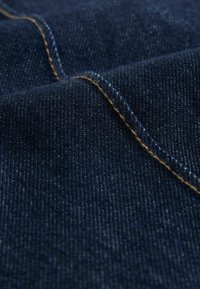 Dunkelblauer Denim-Stoff mit einem subtilen Glanz. Verfügt über kontrastierende, sandfarbene Nähte, die eine feine Textur und diagonale Webmuster zeigen.