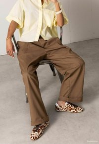 Lichtgele oversized shirt, bruine wijde broek en bruin-witte luipaardprint schoenen met witte accenten. Glad textuur, casual pasvorm.