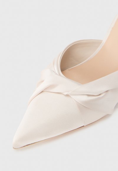 Chaussure à talon haut à bout pointu en satin beige doux, présentant un design noué à l'avant et une finition lisse et polie.