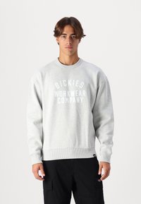 Felpa grigia chiara con polsini e bordo a coste, caratterizzata da un audace logo bianco "DICKIES WORKWEAR COMPANY" sul davanti.
