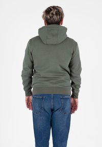 Felpa con cappuccio di un verde tenue, realizzata in tessuto morbido. Presenta polsini e orlo a coste, mostrata indossata con jeans di denim blu di spalle.