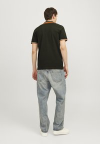 Donkergroene polo met contrasterende oranje en witte kraagaccenten, gecombineerd met lichtblauwe denimjeans en witte sneakers.
