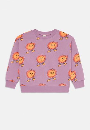 Lilla genser laget av bomull, med et heltrykk av oransje tegneserieblomster som smiler, lange ermer og ribbestrikkede manchetter.
