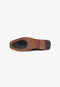 Suela de zapato de cuero marrón con un acabado liso, que presenta detalles en goma negra y costuras visibles a lo largo de los bordes.