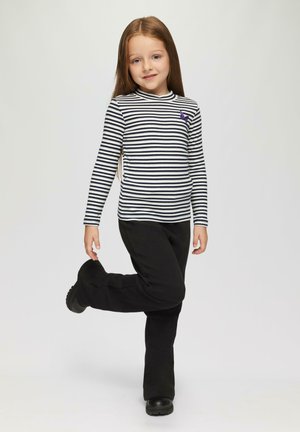 Zwarte flarebroek gecombineerd met een langemouwenshirt met zwart-witte strepen en een paarse vlinderpatch op de borst.