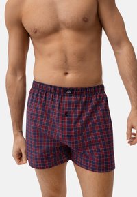 Kostka w kratkę wykonana z mieszanki bawełny w kolorze granatowym z czerwonymi i białymi liniami. Posiada elastyczny pas i pojedyncze zapięcie na guzik.