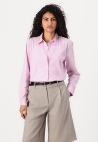 Light pink long-sleeve shirt with blue vertical stripes, button-down collar, paired with beige high-waisted shorts and a black belt.