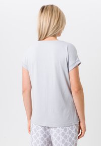 Lichtgrijs t-shirt met korte mouwen en een ronde halslijn, zachte textuur en opgerolde mouwen. G gedragen met gemusterde witte pyjamabroeken.