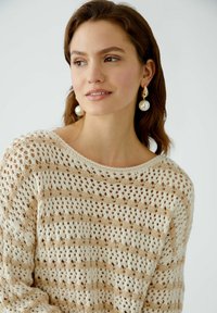 Cremefarbener und beige gestrickter Pullover mit offener Maschenstruktur und gestreiftem Muster, der einen weiten Ausschnitt und lange Ärmel hat.