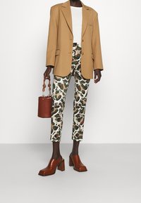 Blazer marron ajusté sur un top blanc, associé à un pantalon à motif camouflage, des mules à talons épais marron et un sac à main circulaire marron.