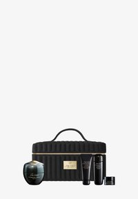 Custodia da viaggio nera trapuntata con logo dorato; contiene quattro prodotti skincare Shiseido: un barattolo di crema, due tubetti e un barattolo piccolo.