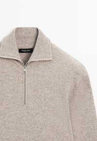 Maglione beige lavorato a maglia con collo a mezzaluna con zip, trama a coste e motivo sottile. Etichetta con scritto "Massimo Dutti". Finitura del tessuto liscia.