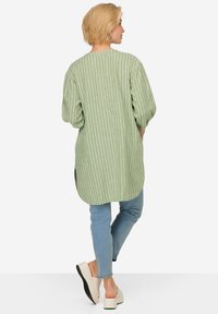 Blusa a righe verdi con un taglio relax, dotata di maniche a tre quarti, orlo arrotondato e spacchi laterali. Abbinata a jeans azzurri chiari e scarpe chiare.