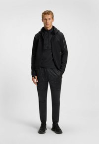 Svart träningsoutfit med en zip-up jacka med huva, fuktavvisande tyg, mönstrad t-shirt och matchande smala byxor.