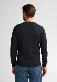 Dunkelblauer Strickpullover mit Rundhalsausschnitt, gerippten Bündchen und Saum, kombiniert mit hellblauen Jeans. Glatte Textur, keine Muster oder Akzente.