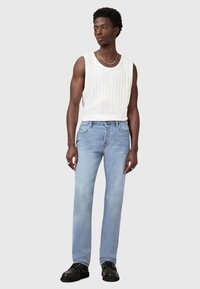 Top in cotone bianco a costine, jeans dritti azzurri chiari e scarpe nere stringate. Collana a catena visibile. Design semplice, look casual.