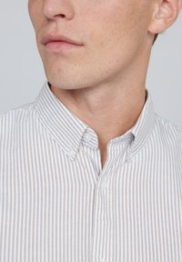 Hemdkragen in Weiß mit hellbraunen vertikalen Streifen, mit einem Button-Down-Kragen und Knopfverschluss auf der Vorderseite.