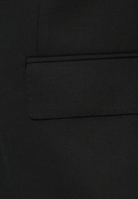 Tissu noir avec une texture lisse, comportant une poche rectangulaire avec un contour cousu, présentant un subtil motif diagonal.