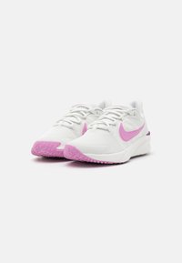 Baskets de sport blanches avec des dessus texturés, des accents roses sur les côtés et les semelles, et un talon rembourré pour le confort et le soutien.