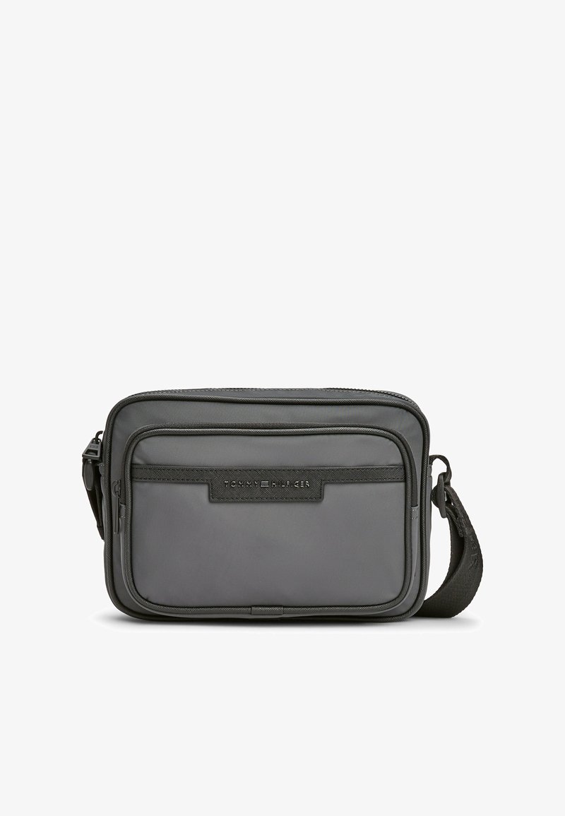 Borsa a tracolla grigia in nylon con tracolla regolabile, dotata di una tasca anteriore con zip e un'etichetta logo testurizzata. Design compatto e rettangolare.